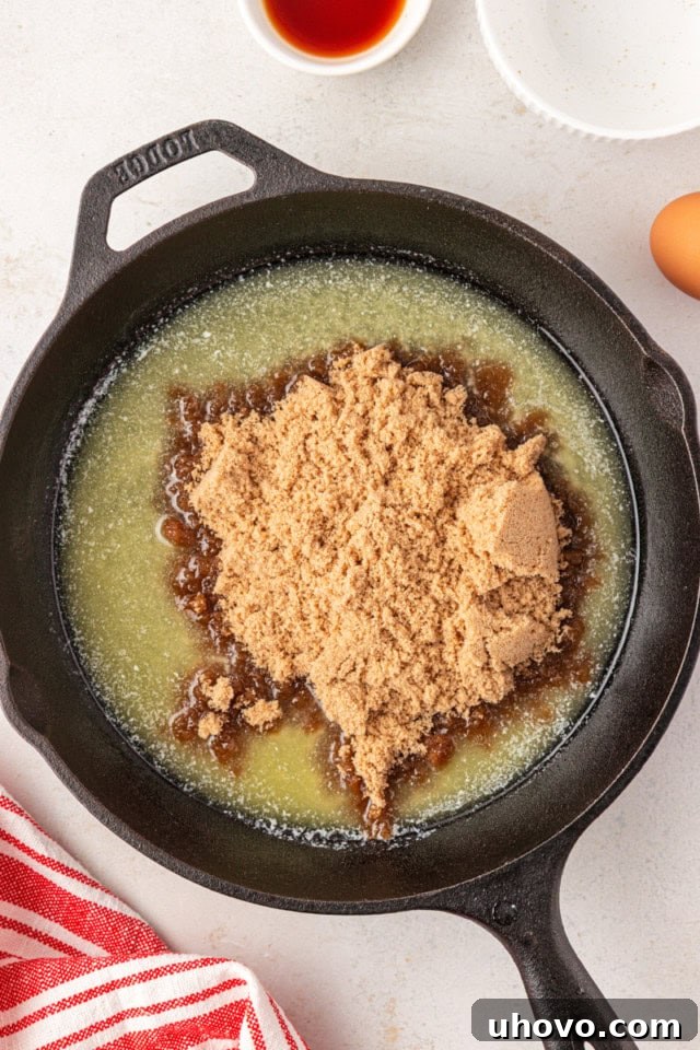 overhead view of brown sugar added to melted butter in a cast iron skillet