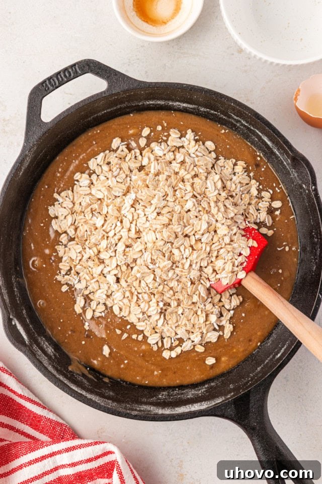 overhead view of oats added to cookie dough in a cast iron skillet