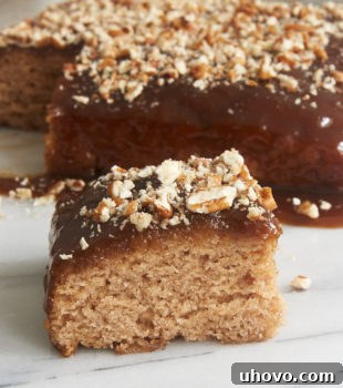 A piece of Cinnamon Pudding Cake on a marble slab, with the remaining cake in the background, showing its gooey sauce.