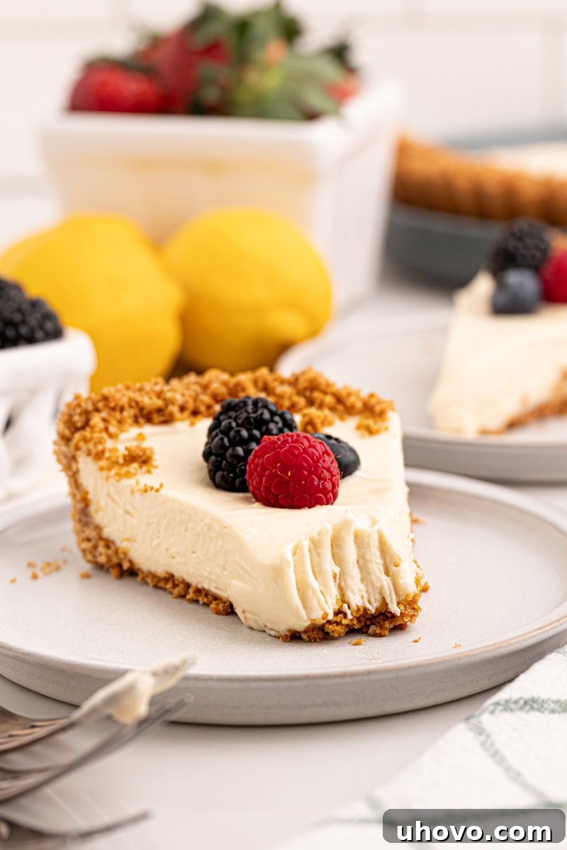 A close-up shot of a slice of lemon cream pie on a white plate, with a perfect bite taken from the front, revealing its creamy layers. In the blurred background, the rest of the pie, whole lemons, and fresh berries are visible, creating a tempting and inviting scene that highlights the deliciousness of the dessert.