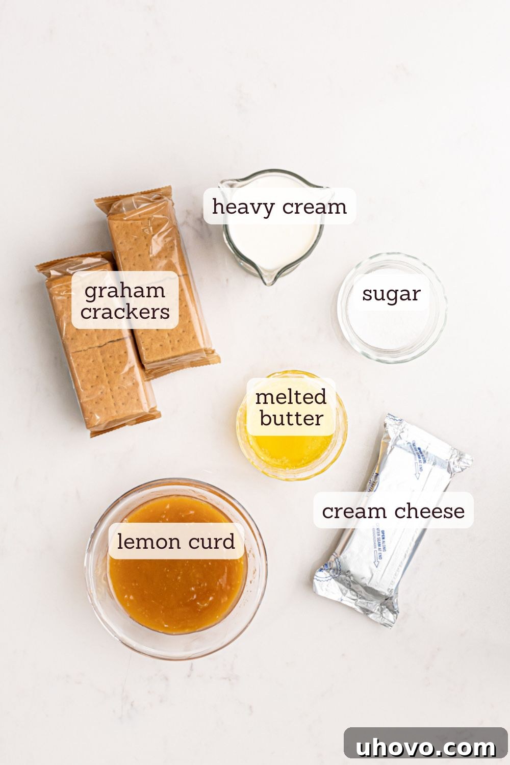 An overhead shot showcasing the essential ingredients neatly arranged for a lemon cream pie. The key components include vibrant yellow lemons, a tub of creamy lemon curd, a block of softened cream cheese, and a carton of heavy cream, all set against a rustic wooden background.