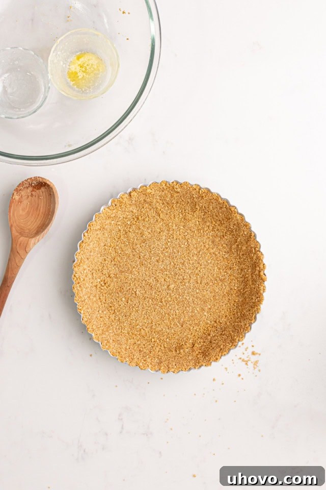 An overhead view of the completed graham cracker crust, firmly pressed into a traditional metal pie pan. The crust extends evenly up the sides and across the bottom, forming a perfect base for the pie filling.