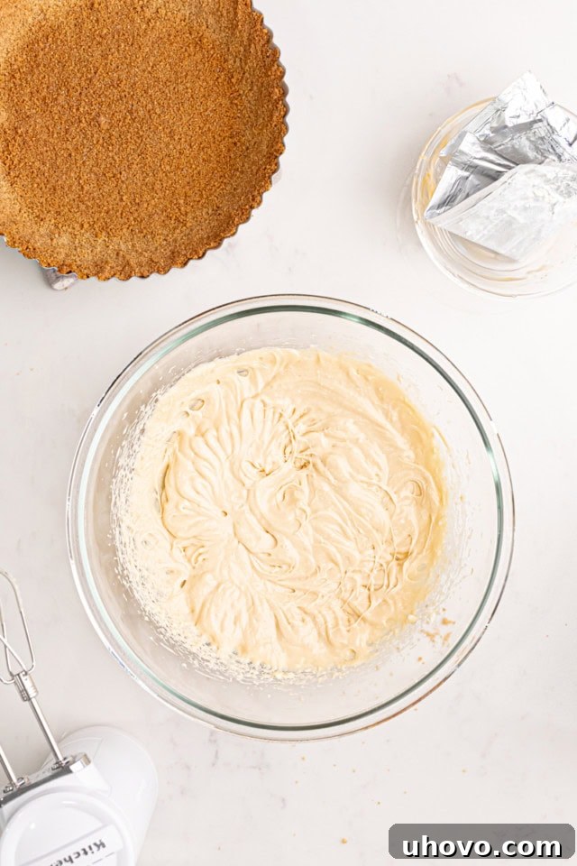 An overhead view of a clear glass mixing bowl containing a light yellow mixture of beaten lemon curd and cream cheese. The ingredients are perfectly blended, showcasing a smooth, uniform, and creamy texture.