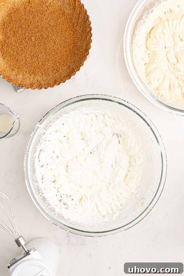 An overhead view of a clear glass mixing bowl filled with perfectly whipped heavy cream, showcasing distinct soft peaks. The cream is light, airy, and holds its shape gently, indicating it's ready for folding.