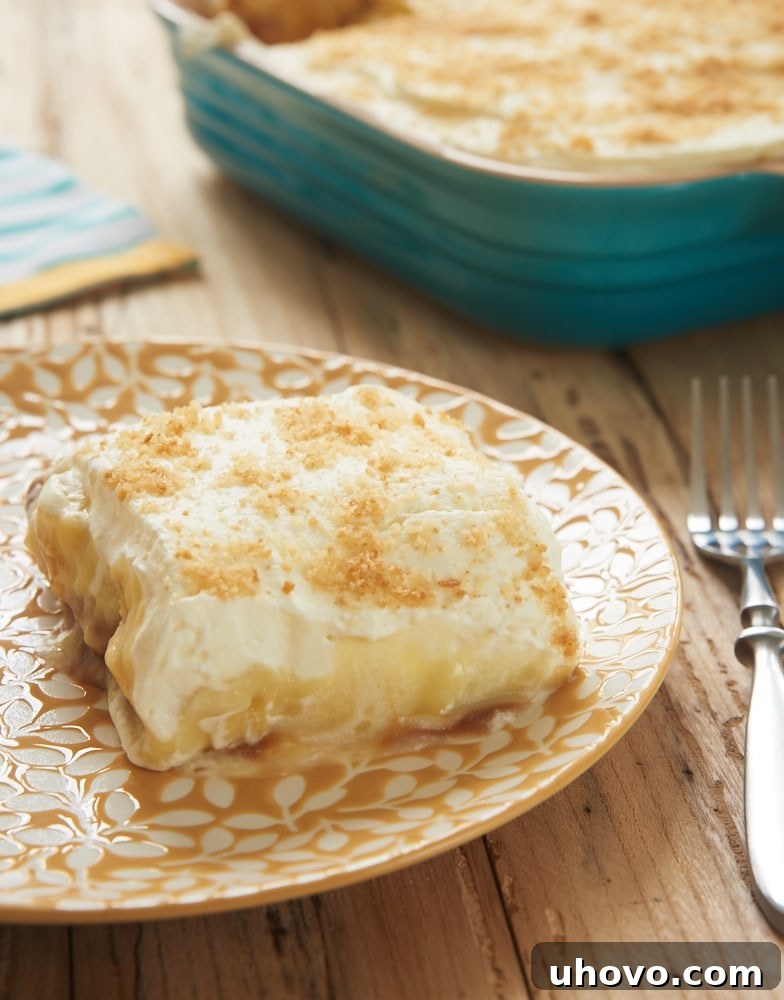 A square of banana pudding bar on a white plate, showcasing its distinct layers and a fork beside it.