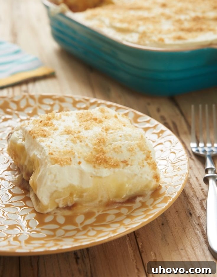 A square of banana pudding bar on a white plate, showcasing its distinct layers and a fork beside it.