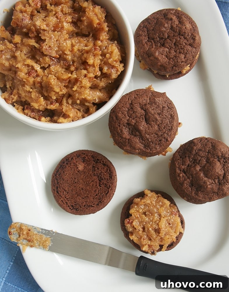 Hands carefully assembling Chocolate Coconut Pecan Sandwich Cookies, showing the generous layer of frosting between two fudgy cookies