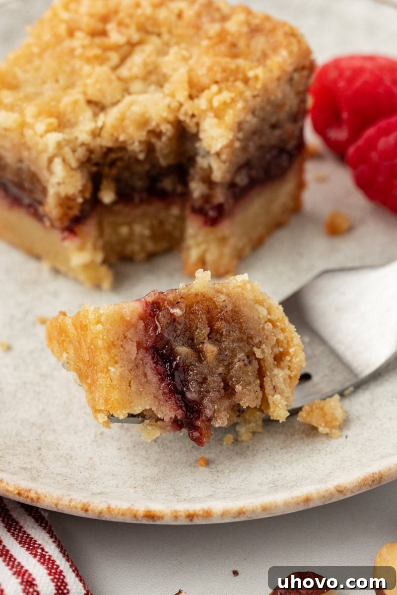 Close-up corner of a raspberry crumble bar on a fork, showing the distinct layers