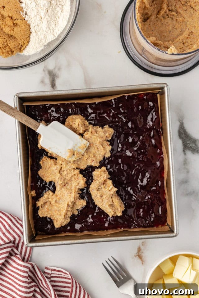 Overhead view of hazelnut layer being spread smoothly over preserves for raspberry crumble bars