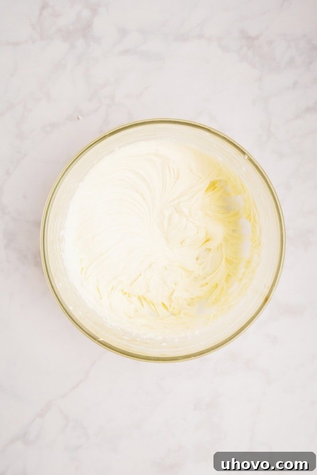 overhead view of mixed cream cheese, sugar, and vanilla in a glass mixing bowl