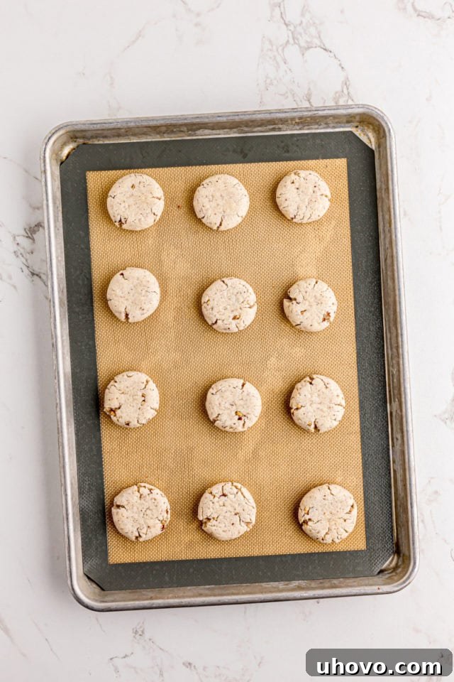 Flattened cream cheese shortbread dough balls on a Silpat-lined baking sheet, ready for the oven.