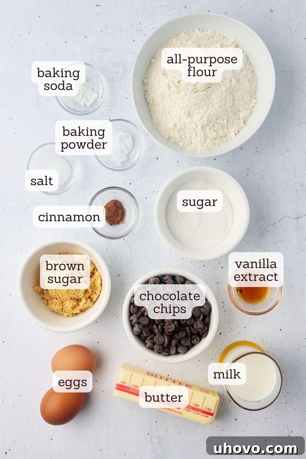Overhead view of perfectly portioned and labeled ingredients for homemade chocolate chip muffins on a white surface, demonstrating readiness for baking.