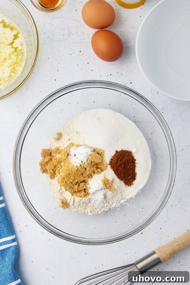 Dry ingredients, including flour, sugar, and leavening agents, being whisked together in a clear glass mixing bowl, forming a perfectly combined foundation for the muffins.