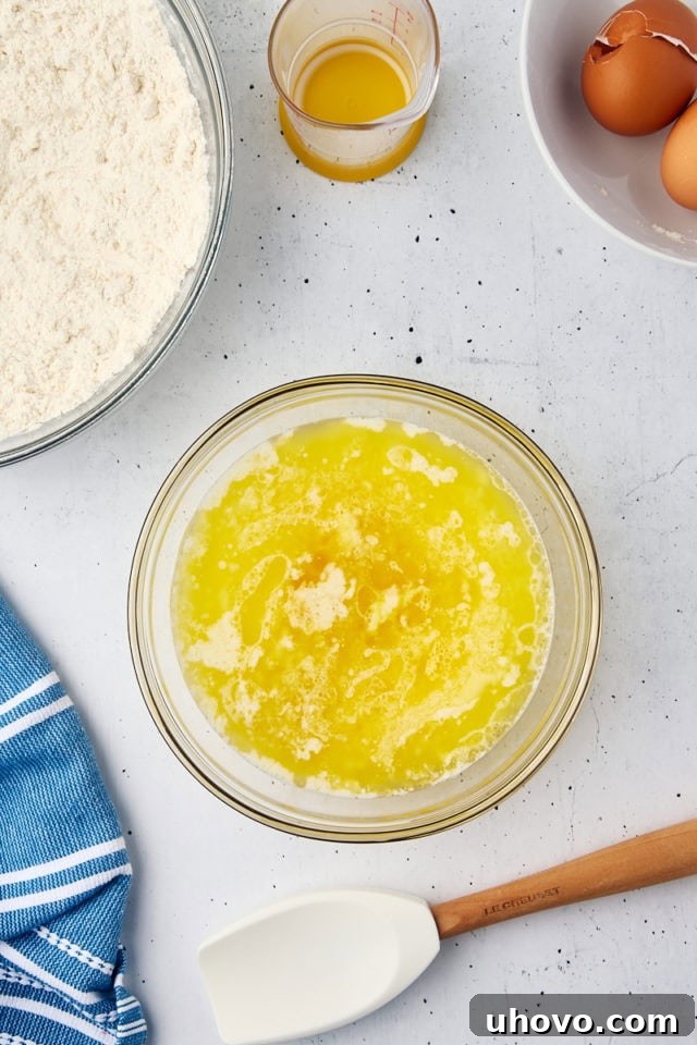 Wet ingredients, including eggs, melted butter, milk, and vanilla extract, stirred together in a separate glass mixing bowl, creating a smooth, liquid mixture.