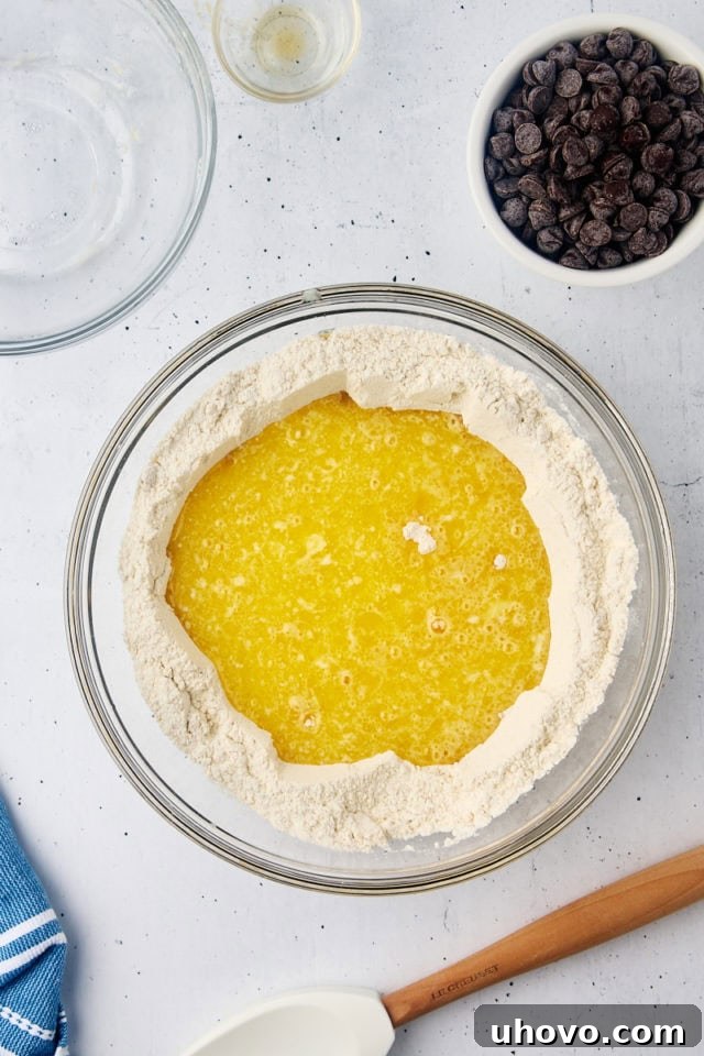 Overhead view of the wet ingredients mixture being carefully poured into the well created in the center of the dry ingredients in a large glass bowl, ready for gentle mixing.