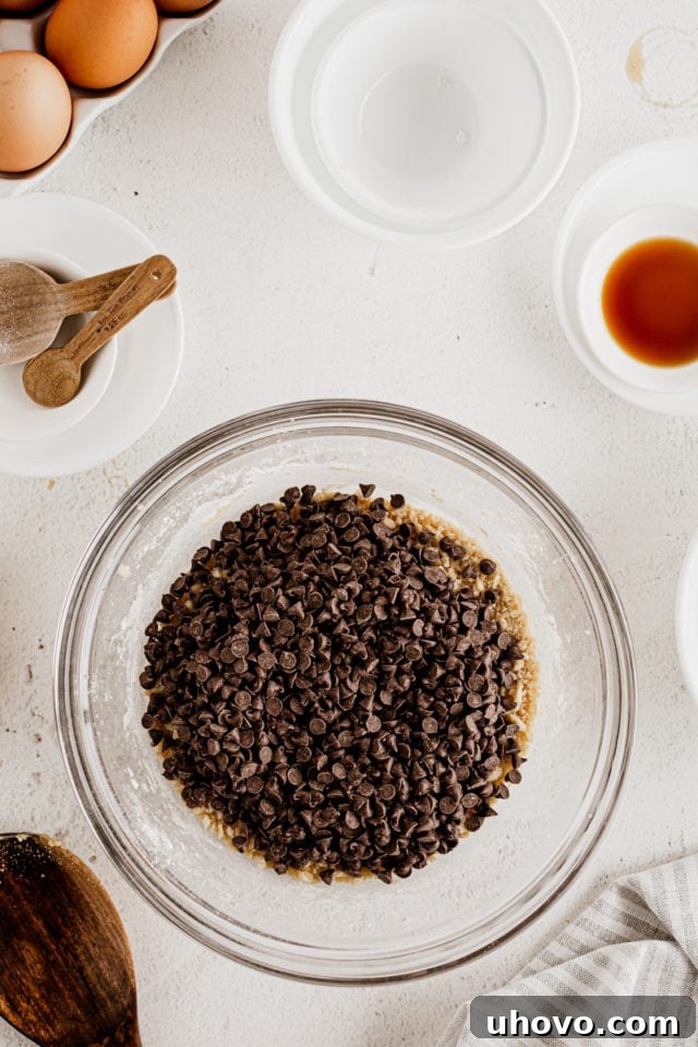 Overhead view of chocolate chips in glass mixing bowl with dough