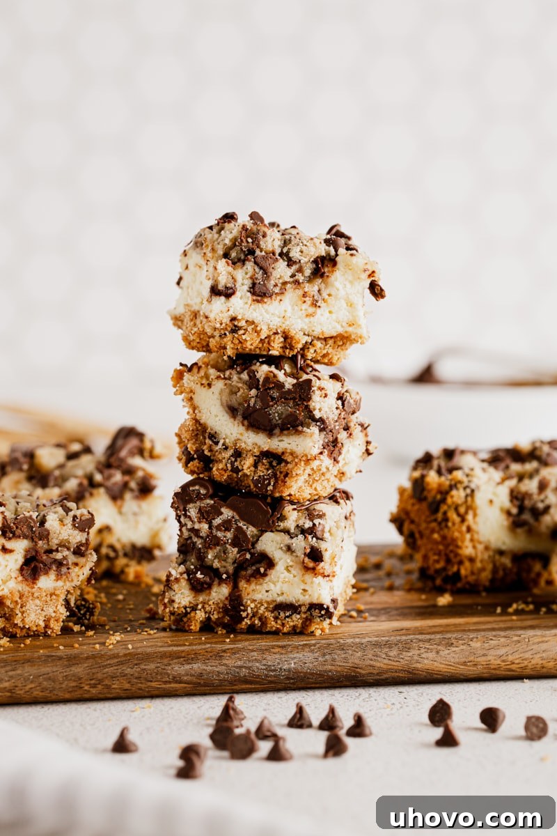 Three cookie dough cheesecake bars stacked on wood board