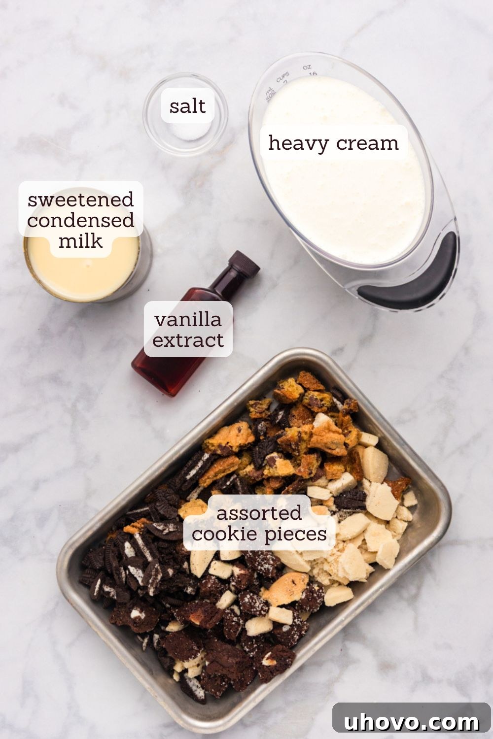 Overhead view of the key ingredients laid out for making All the Cookies Ice Cream: sweetened condensed milk, heavy cream, vanilla extract, salt, and various cookie pieces.
