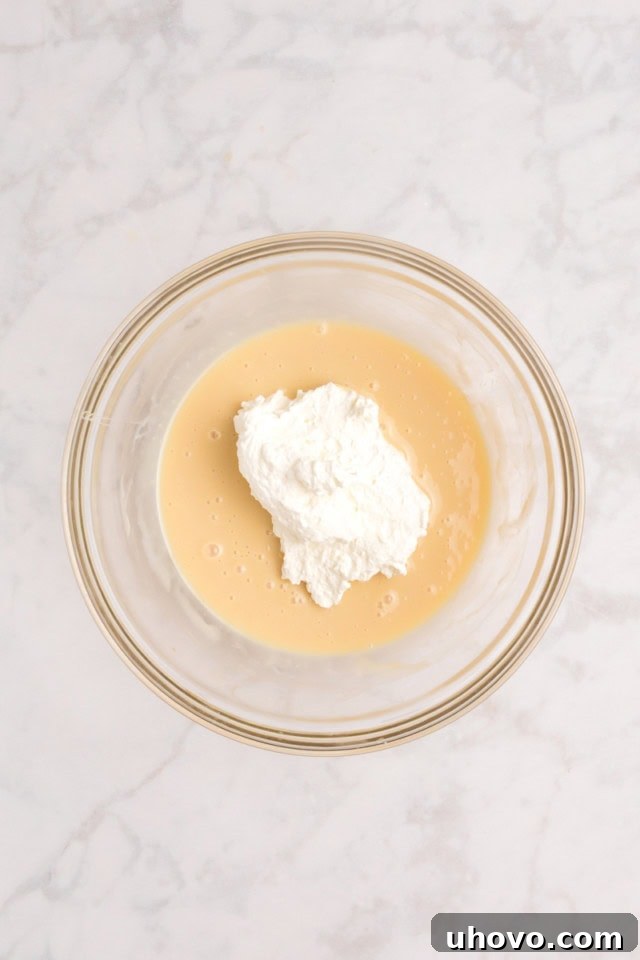 Overhead view of a small amount of whipped cream being gently folded into the sweetened condensed milk mixture for the no-churn ice cream base.
