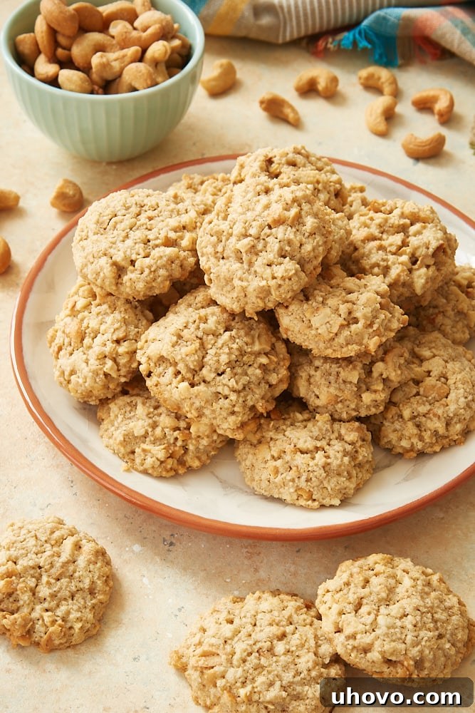 A stack of golden brown Salted Cashew Crunch Cookies on an orange-rimmed white plate, hinting at their delicious texture.