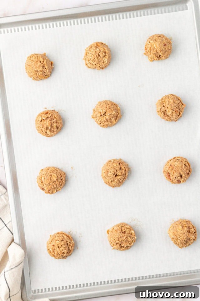 Overhead view of scooped portions of toffee almond oatmeal cookie dough neatly arranged on a prepared baking sheet.