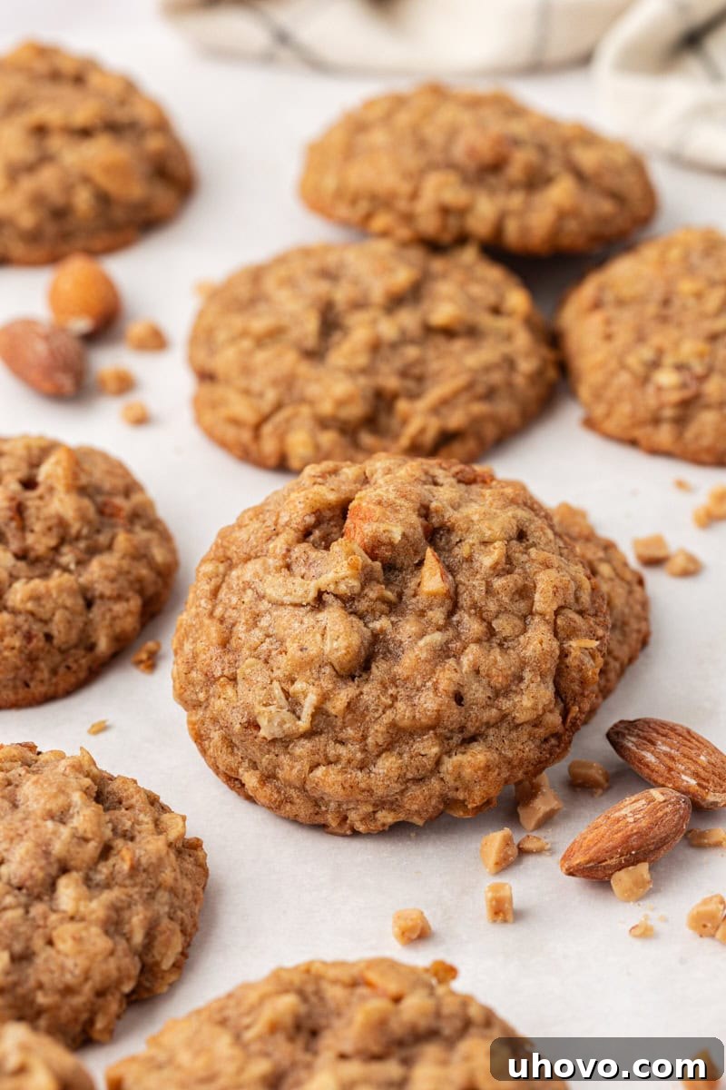 Several toffee almond oatmeal cookies piled on a white countertop, highlighting their golden color and tempting texture.