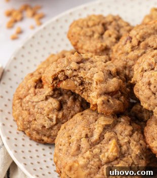 Toffee almond oatmeal cookies piled high on a white plate, with a bite missing from the top cookie revealing its chewy interior.