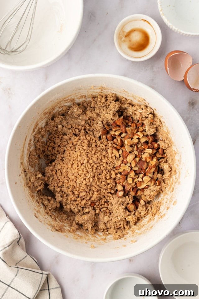 Overhead view of chopped toasted almonds and toffee bits being stirred into the cookie dough.