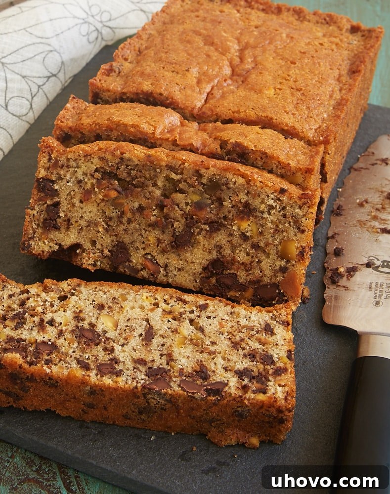 A whole Chocolate Chip Pistachio Pound Cake cooling on a dark cutting board, showcasing its golden crust and delicious texture.