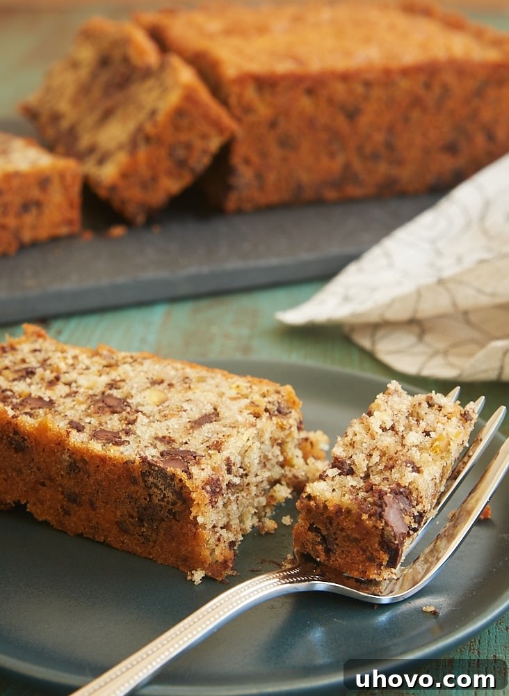 A delicious slice of Chocolate Chip Pistachio Pound Cake served on a dark plate, showing off the generous chocolate chips and green pistachios within.