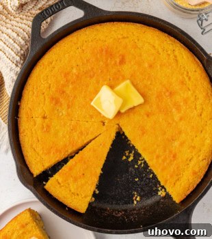 Sour cream corn bread topped with two pats of butter in a cast iron skillet, golden brown and inviting.