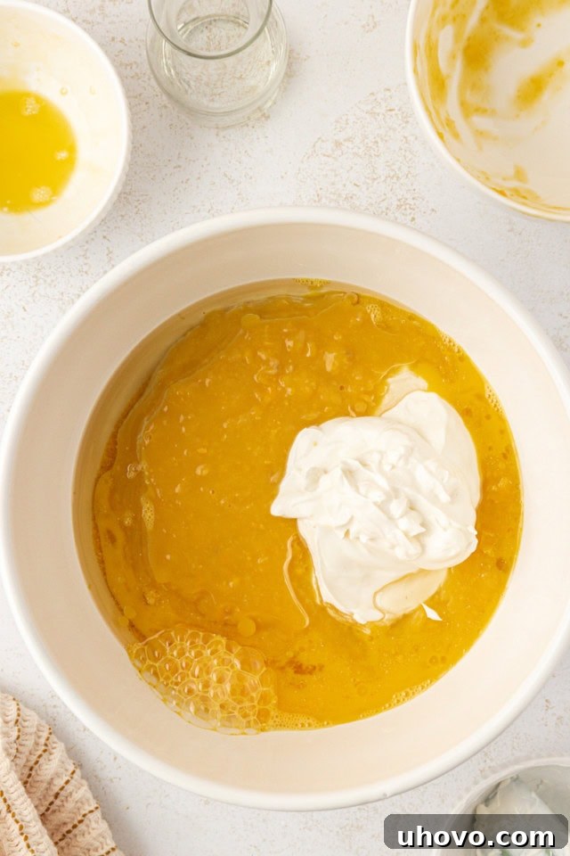 Overhead view of eggs, vegetable oil, sour cream, and cream-style corn in a separate white mixing bowl, ready to be mixed.