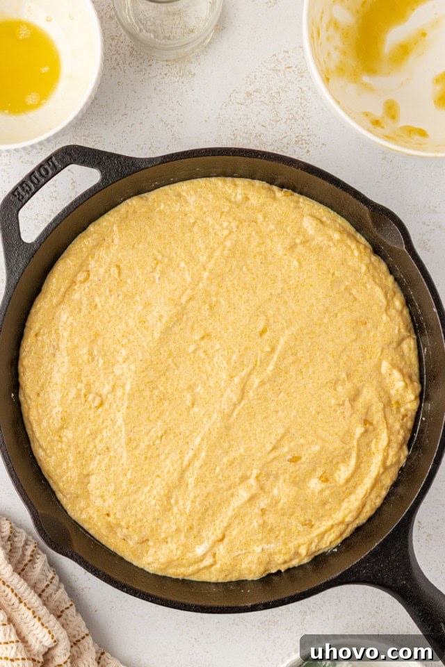 Overhead view of the sour cream corn bread batter spread evenly into a buttered cast iron skillet, ready for the oven.