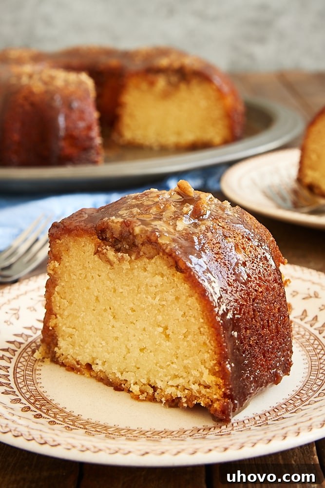 A delectable slice of Pecan Pie Bundt Cake served on a brown floral plate, with the elegantly shaped remaining cake in the background.