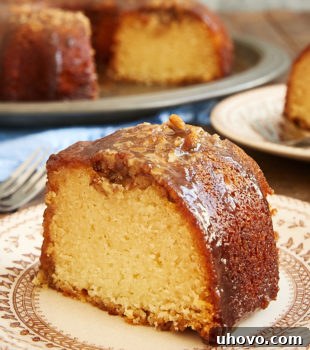 A delicious slice of Pecan Pie Bundt Cake on a brown floral plate with the remaining elegant cake in the background.