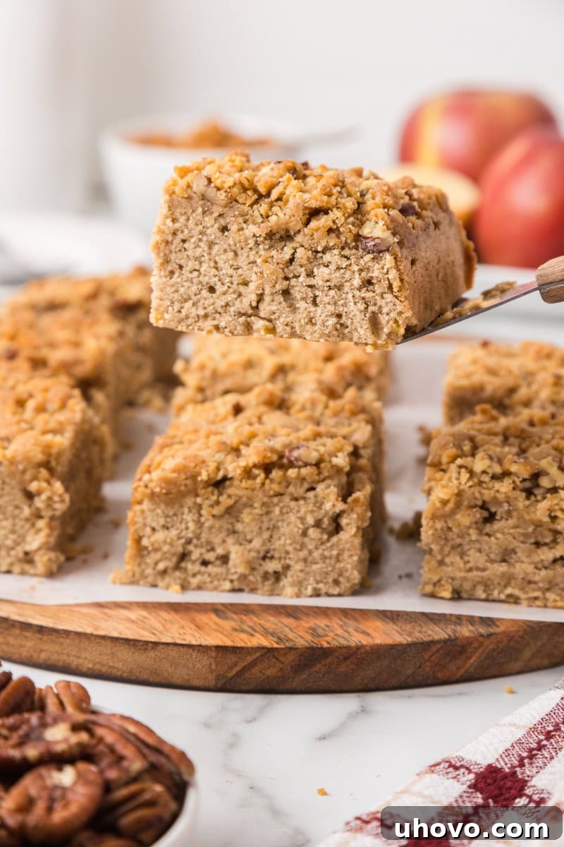 a slice of caramel apple crumb cake on a cake server with the remaining cake in the background