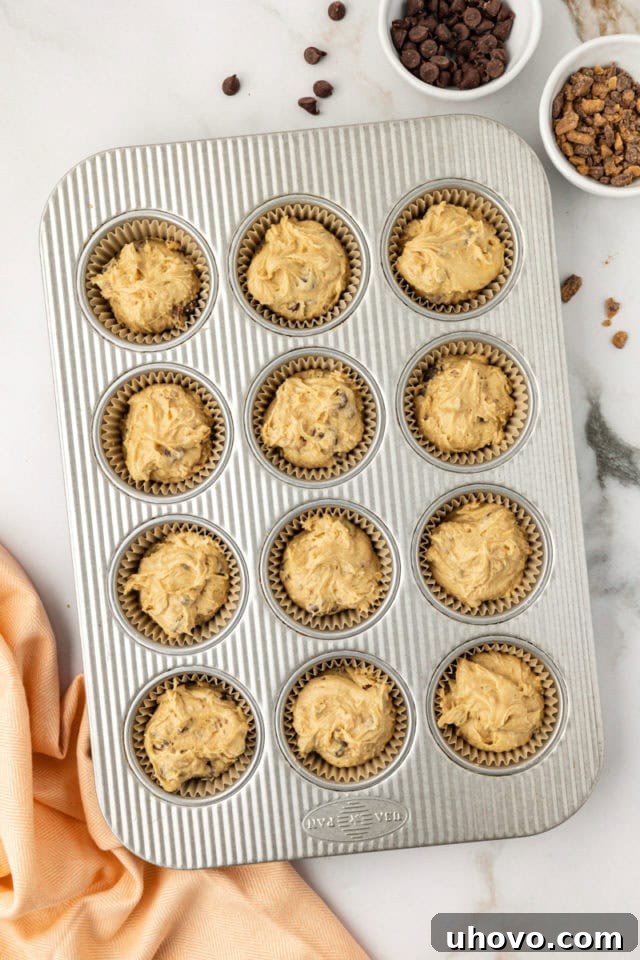 Overhead view of a muffin pan with 12 cups filled evenly with blondie cupcake batter, perfectly portioned and ready to be transferred to the oven for baking.