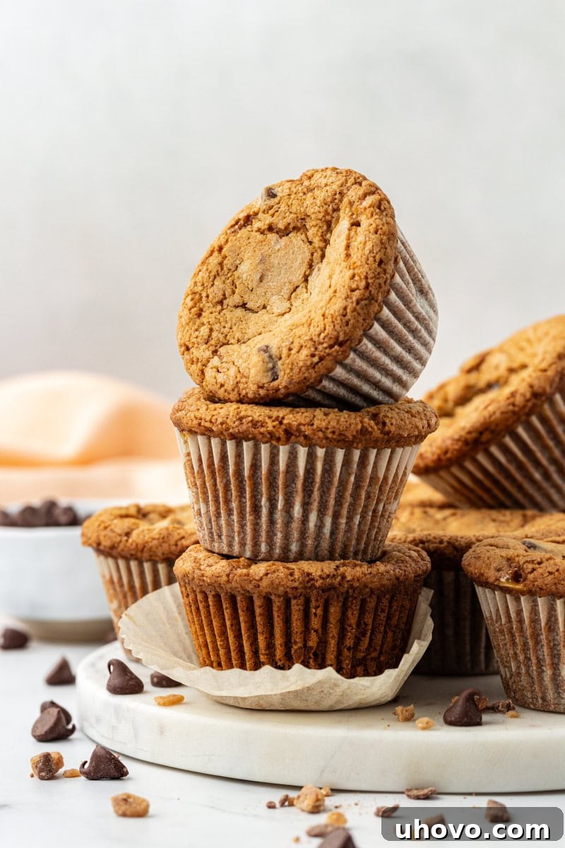 A perfectly balanced stack of three golden-brown blondie cupcakes, richly studded with chocolate and toffee, presented on an elegant marble tray, ready to be enjoyed.