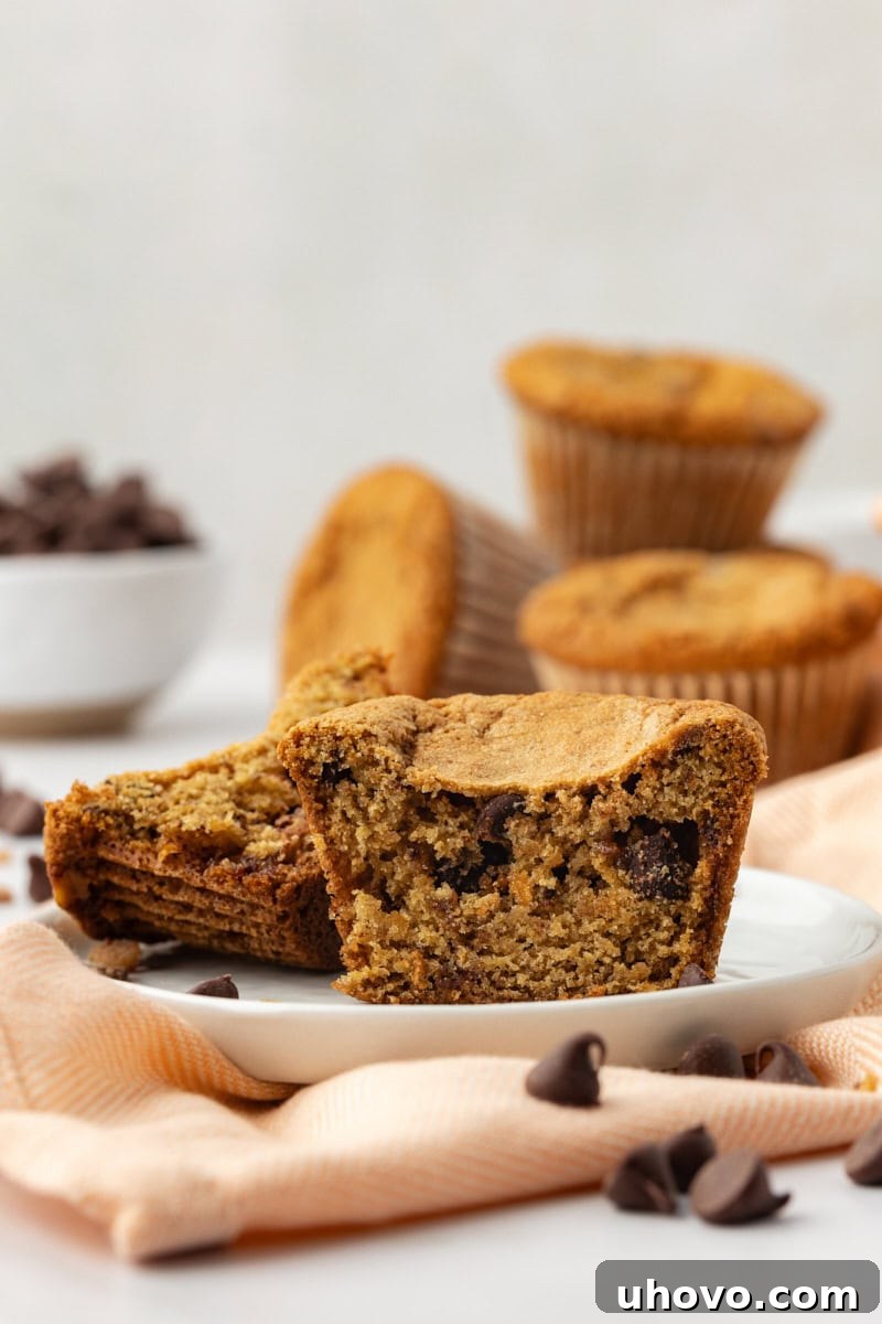 A blondie cupcake meticulously cut in half to reveal its beautifully chewy internal texture, filled with melted chocolate chips and toffee bits, inviting a closer look at its delicious cross-section.