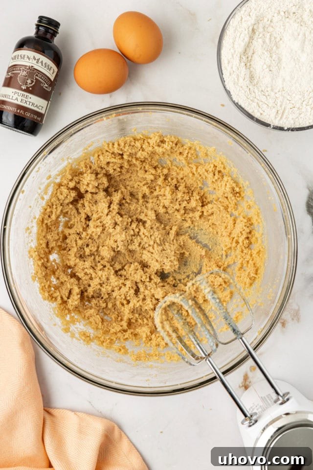 Overhead view of softened unsalted butter and firmly packed brown sugar being creamed together in a clear glass mixing bowl, forming a light and fluffy mixture.