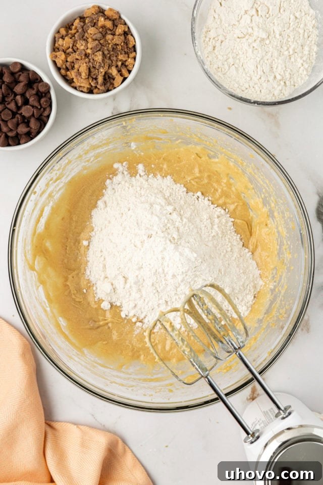 Overhead view of the pre-mixed dry ingredients (flour, baking soda, salt) being gently added to the wet mixture in a glass mixing bowl for blondie cupcakes, ensuring careful combination.