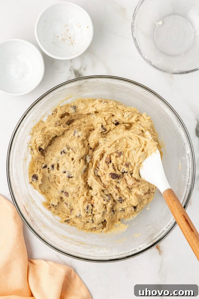 Overhead view of the completed blondie cupcake batter, now uniformly mixed with chocolate chips and toffee bits, resting in a glass mixing bowl, ready for portioning.