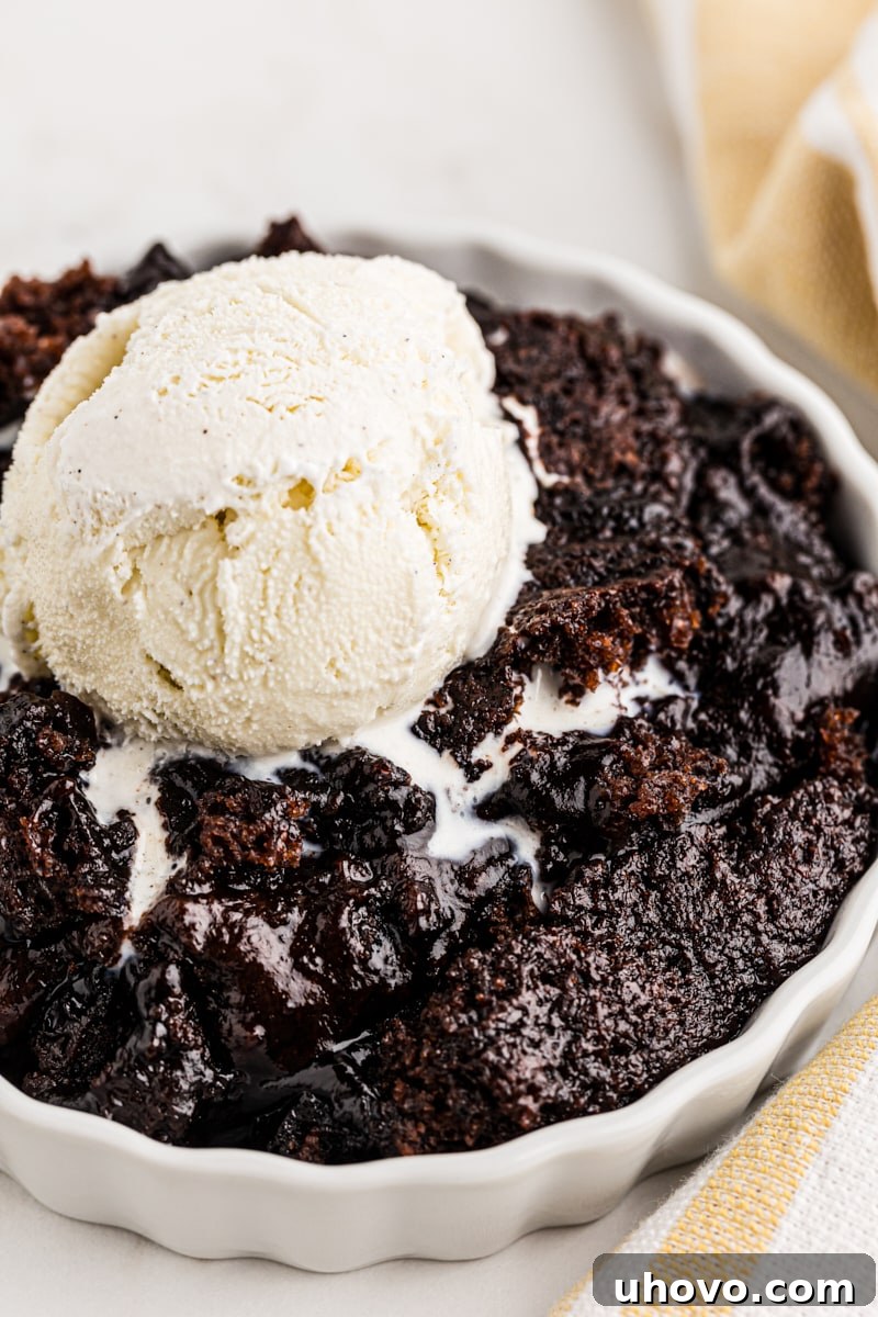 Close-up of a single serving of chocolate cobbler in a ramekin, topped with a scoop of melting vanilla ice cream and glistening with rich chocolate sauce.
