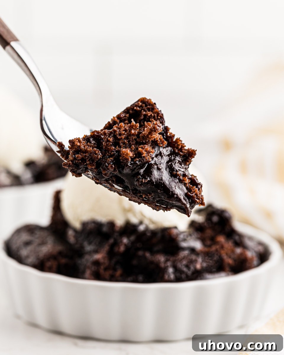 A spoonful of warm chocolate cobbler, showcasing the rich cake and gooey chocolate sauce, lifted from the baking dish.