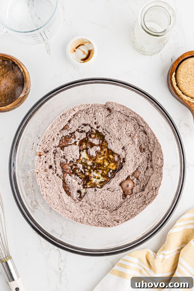 Overhead view of wet ingredients being combined with dry ingredients in a mixing bowl to form the cobbler batter.