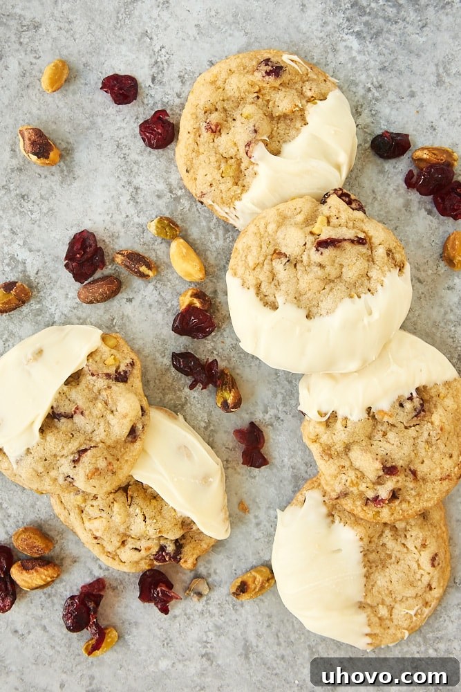 Close-up overhead view of golden-baked Cranberry Pistachio Cookies on a neutral gray surface, showcasing the vibrant red cranberries and green pistachios.
