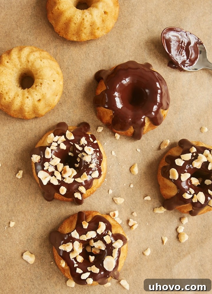 Close-up of Brown Butter Hazelnut Bundt Cakes being topped with rich dark chocolate ganache and sprinkled with chopped hazelnuts.