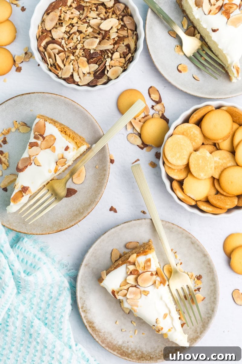 An inviting overhead view of two slices of Amaretto Cheesecake on elegant white plates, garnished with toasted almond slivers and whole vanilla wafers, evoking a sense of celebration.