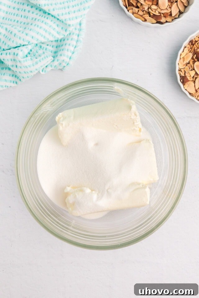 Close-up, overhead view of softened cream cheese and granulated sugar in a clear glass mixing bowl, ready to be beaten together into a smooth mixture.