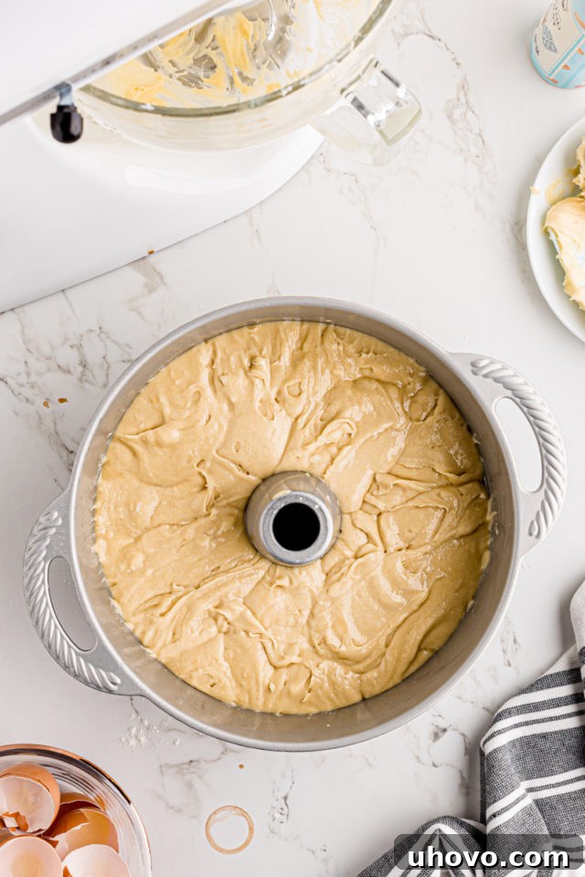 Smooth cream cheese pound cake batter meticulously spread evenly into a prepared tube pan, ready for baking.